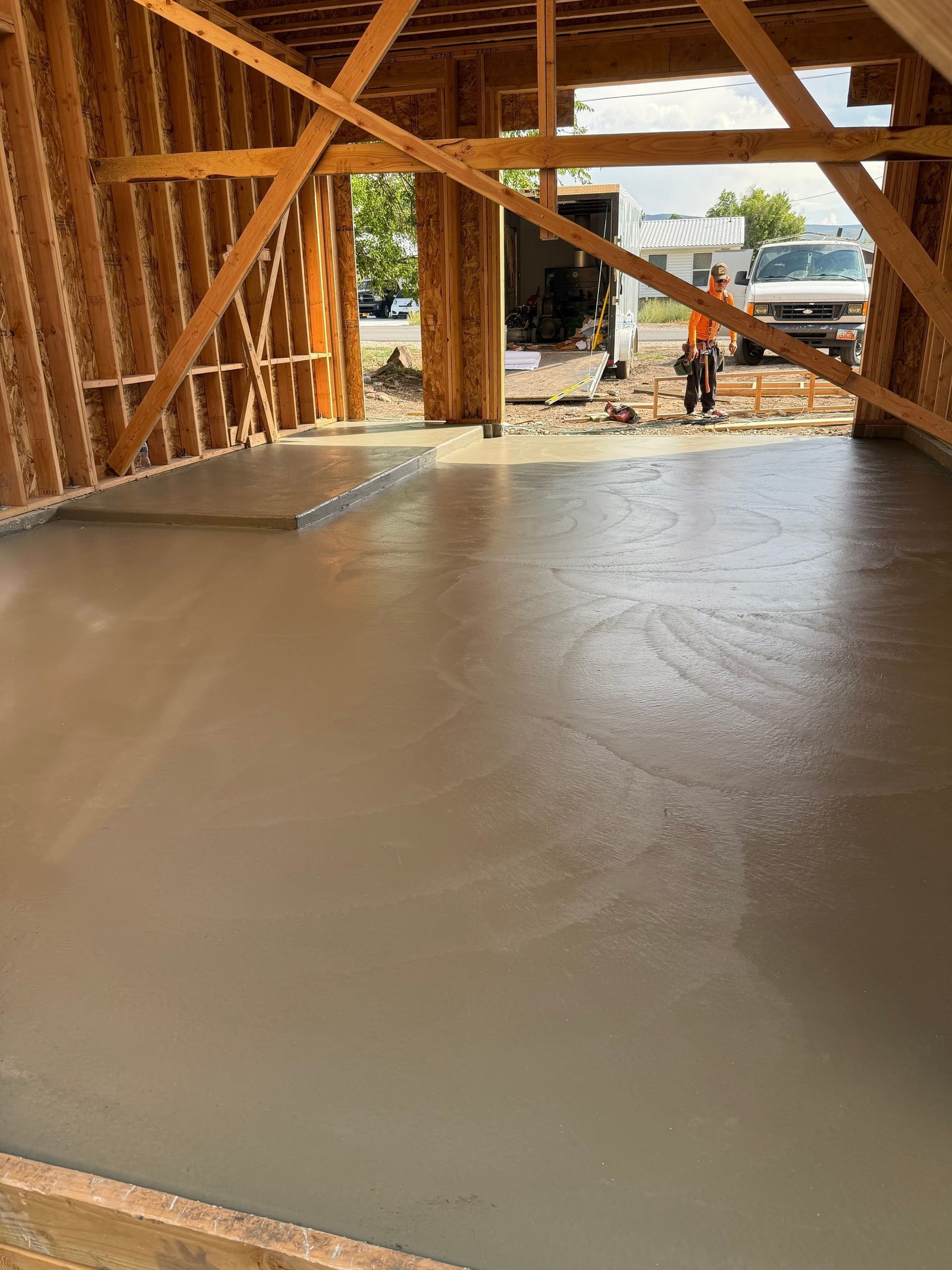 Newly poured concrete floor inside a wooden frame building under construction.